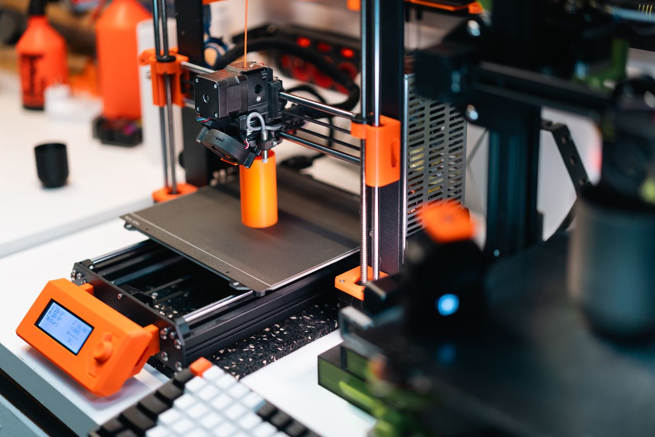 Mastering the First Impression: Your intriguing post title goes here 3D printer operating in a workshop, creating a prototype with orange accents.